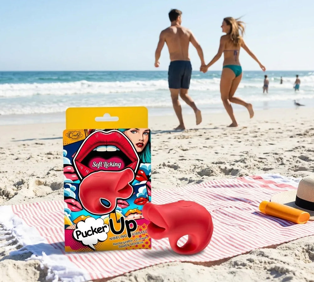 Pucker Up Lips With Ergonomic Finger Hold Vibrator Red on a beach with a couple walking in the background.