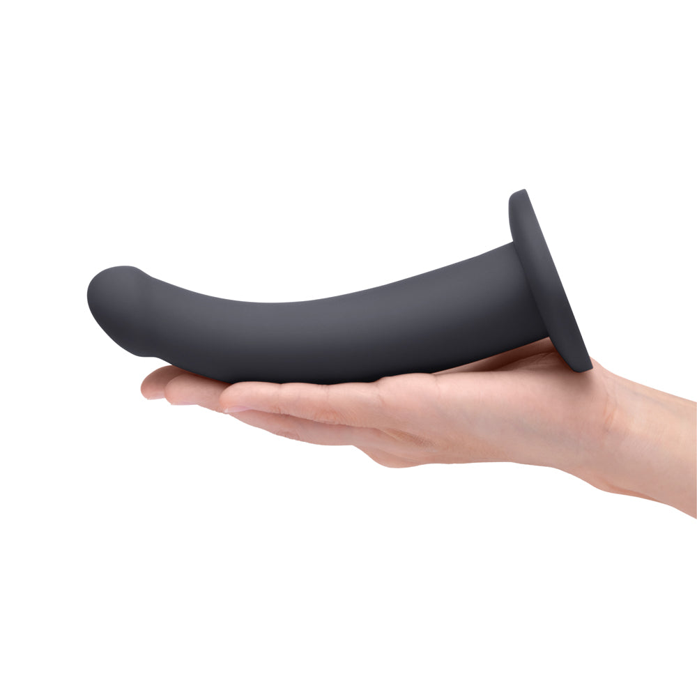 B-vibe Essentials 7 Inch Smooth Silicone Dildo Black held in a hand, showcasing its sleek design.