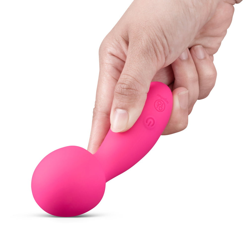 A hand holding the Together Spark On The Go Mini Wand Vibrator, showcasing its vibrant pink color and sleek design.