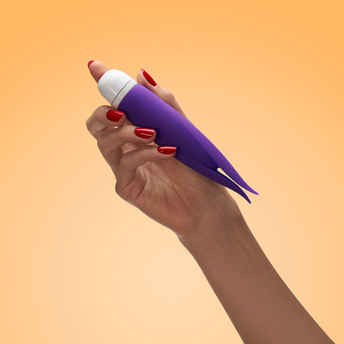 Hand holding Fun Factory Volita Vibrator Violet with red nails against a warm orange background.