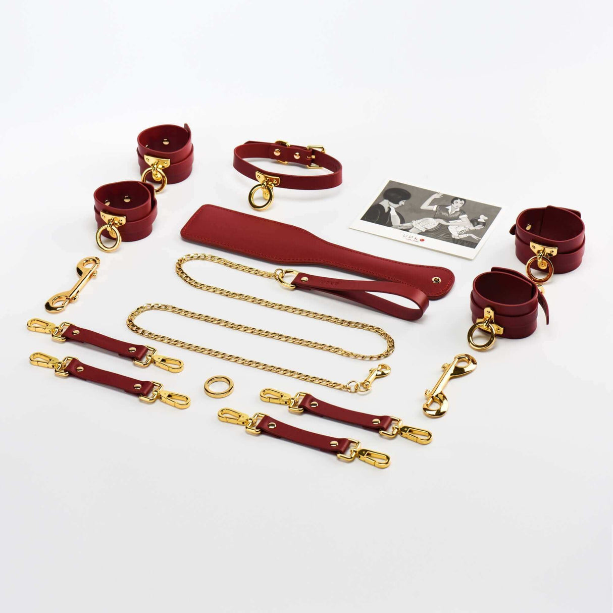 Luxury red Italian leather bondage tools set with gold accents, including cuffs, leash, and accessories in a polished arrangement.