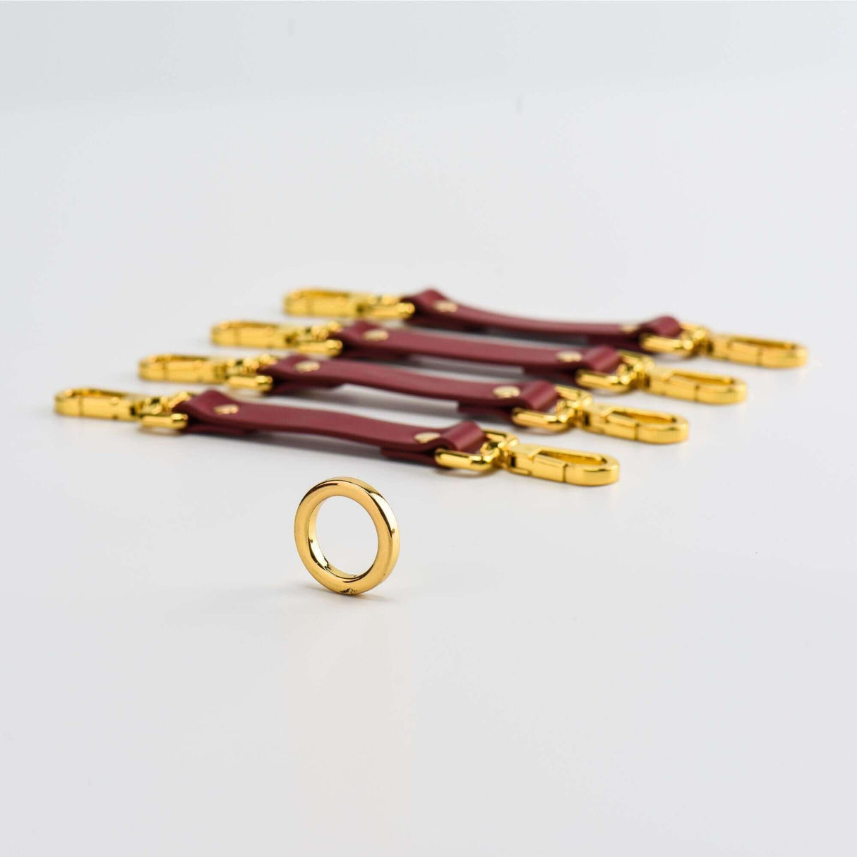 Luxury red leather bondage wrist cuffs with gold hardware and a metal ring, part of the UPKO Italian leather tools set.