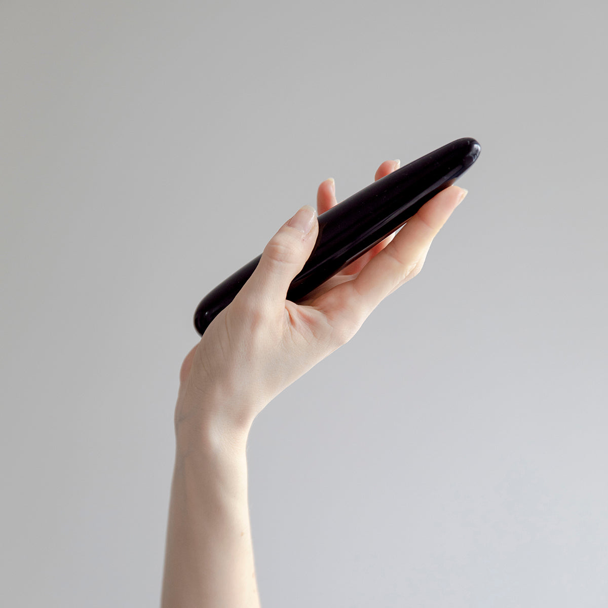 Chakrubs Xaga Slim Non-Phallic Dildo held in a hand against a minimalist background.