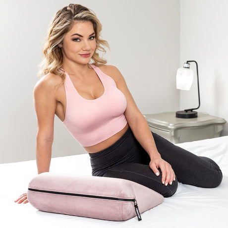 Liberator Jaz Original Rose Sex Pillow on bed with a woman in a pink top demonstrating its use and design.