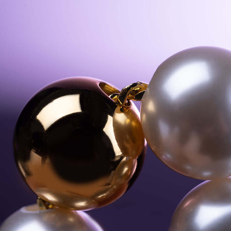 Close-up of UPKO "Moist Eyes" pearl bracelet handcuffs with gold and pearl details against a purple background.