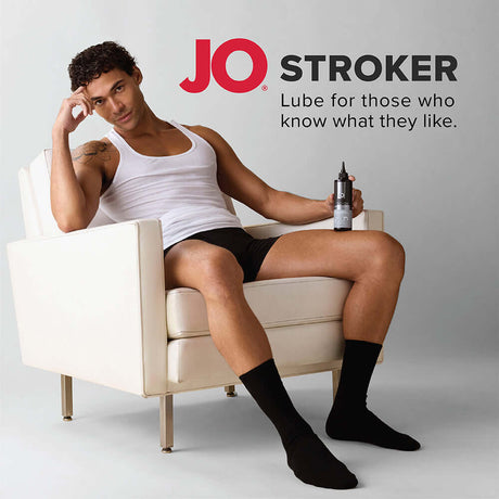 JO Stroker Lubricant 4 Oz bottle held by a man sitting on a chair, promoting enhanced pleasure.
