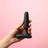 Hand holding Lovense Glint Touch-Responsive Vibrating Butt Plug Black against a pink background.
