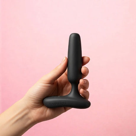 Hand holding Lovense Glint Touch-Responsive Vibrating Butt Plug Black against a pink background.