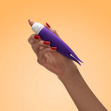 Hand holding Fun Factory Volita Vibrator Violet with red nails against a warm orange background.