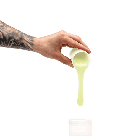 Hand pouring light green silicone from a cup, showcasing the Clone-A-Willy Silicone Refill Glow In The Dark Green.
