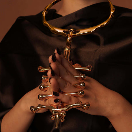 Hands holding a gold UPKO migratory bird metal collar and finger clamps set, showcasing modern luxury and artistic design.
