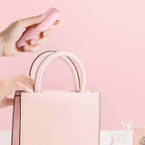Hand holding Sweet Secret Dual Massager Pink above a stylish pink handbag.