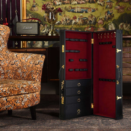 Luxury bondage trunk with red velvet lining and storage slots for BDSM tools, positioned next to a stylish armchair.